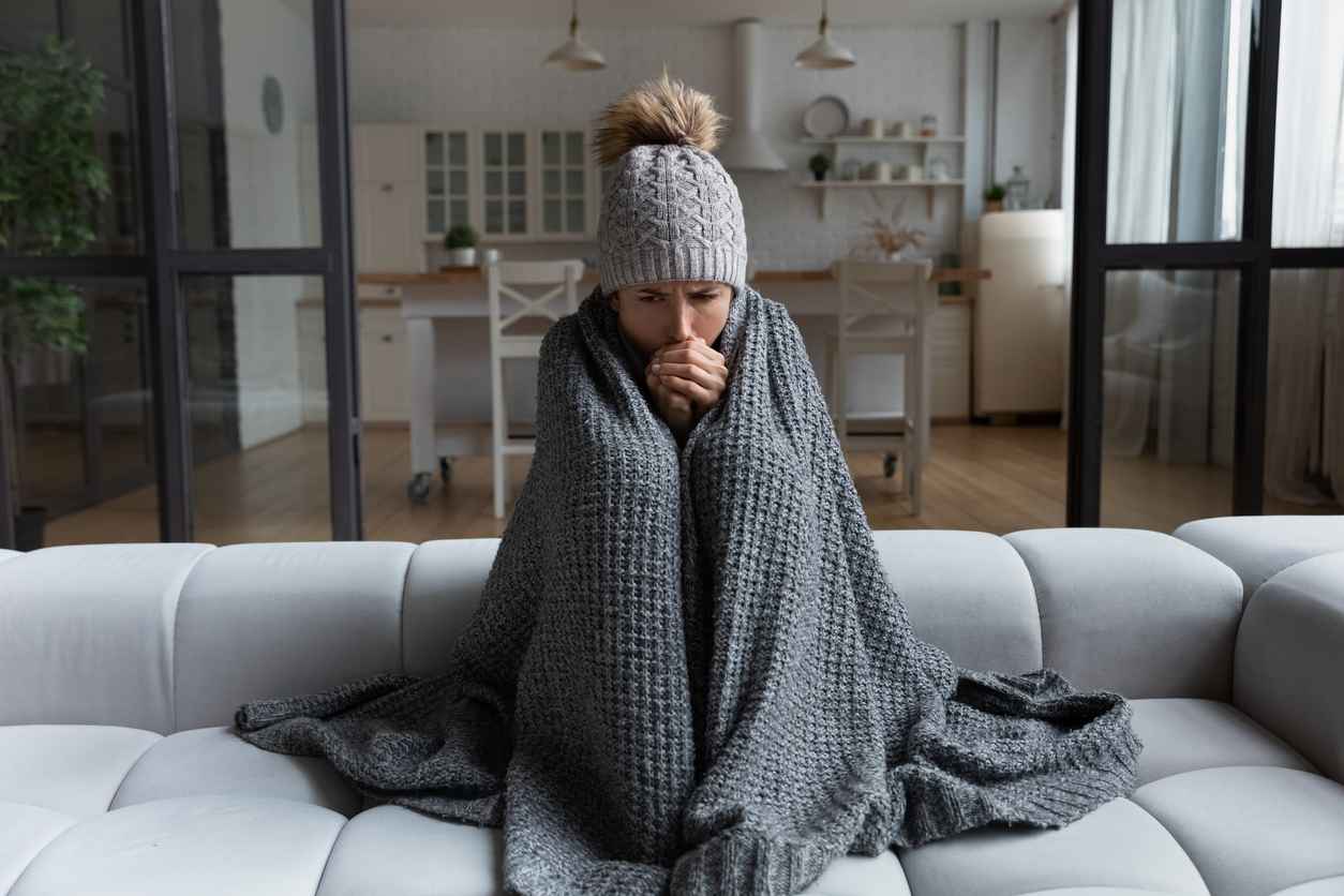 Woman wrapped in a blanket on the sofa to keep herself warm due to a broken furnace.