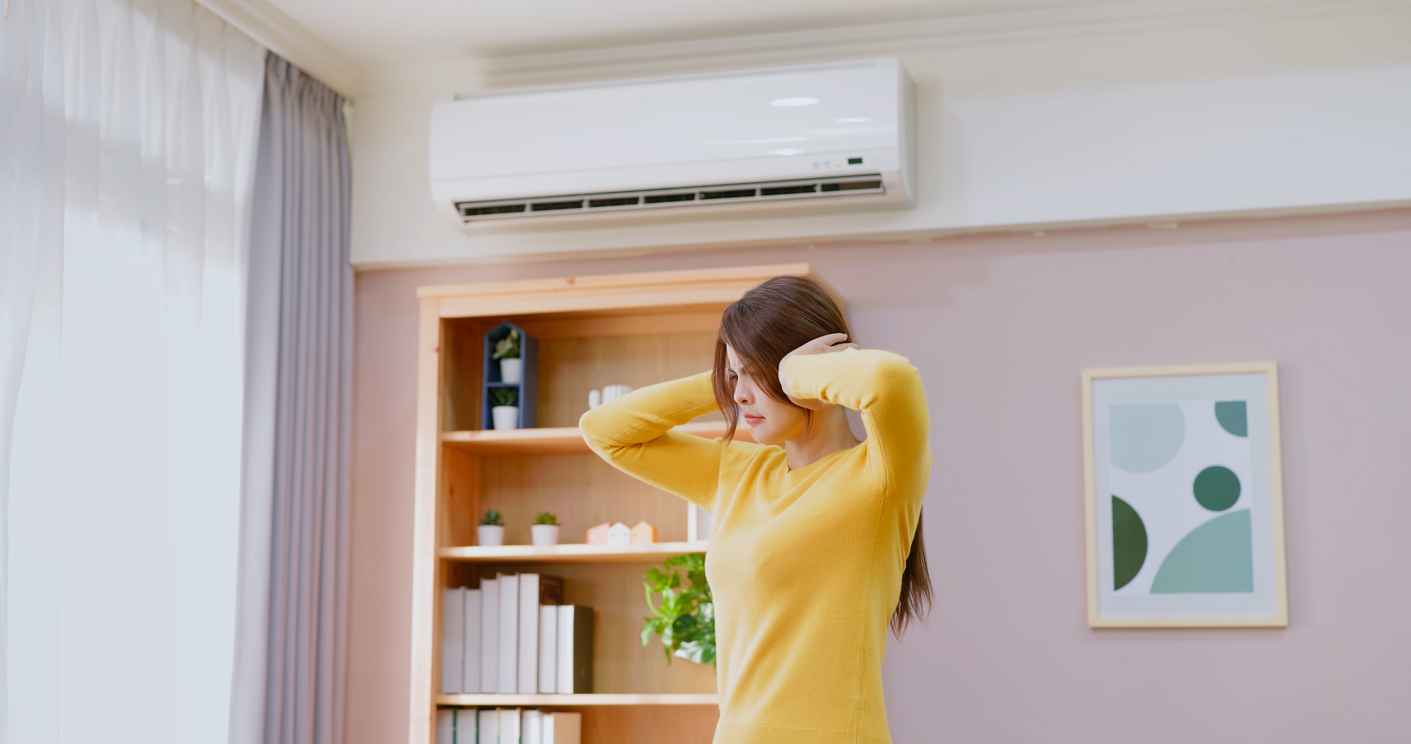 Woman feeling annoyed and covering her ears because her air conditioner is making a loud noise