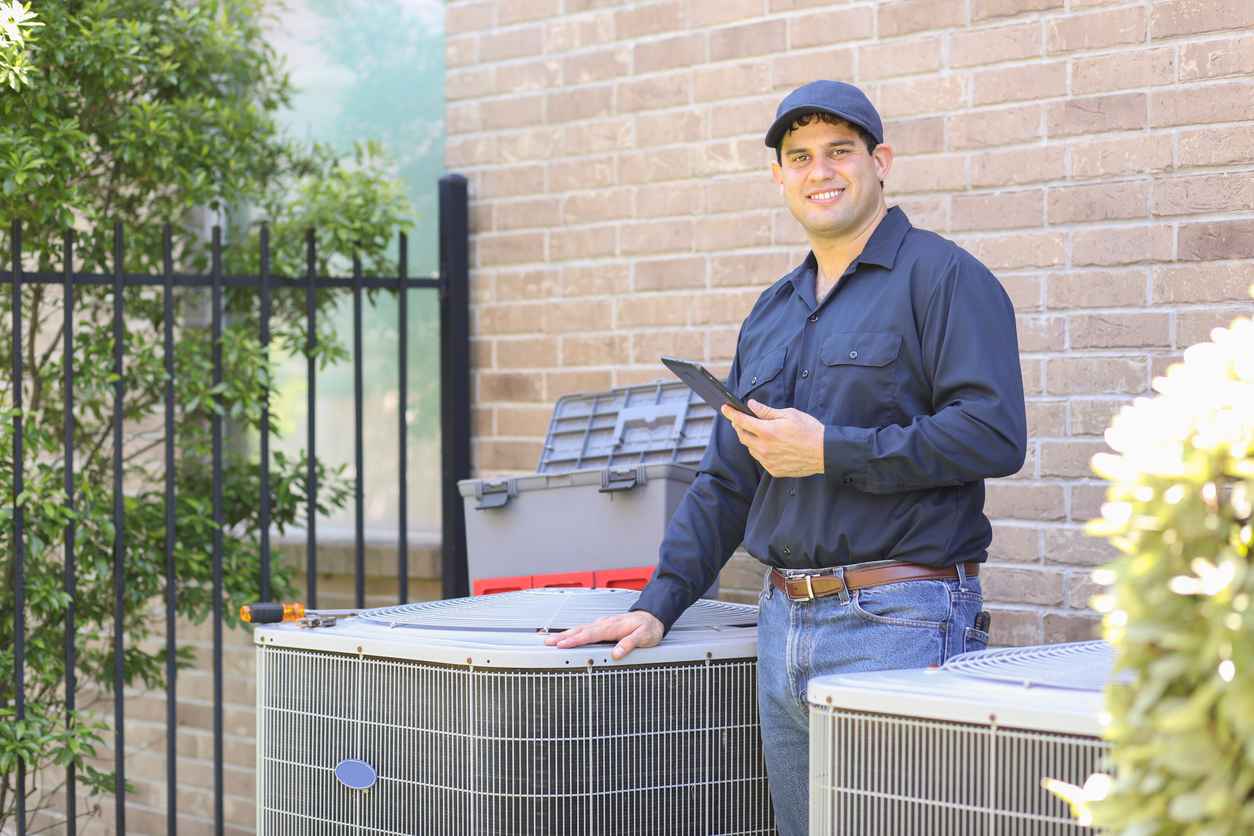 Air conditioner repairman working at residential home. He prepares to begin work by gathering appropriate tools and referring to digital tablet.